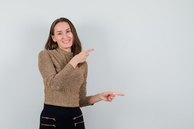 Jeune femme en chemisier doré pointant de côté et à la joyeuse, vue de face. espace pour le texte