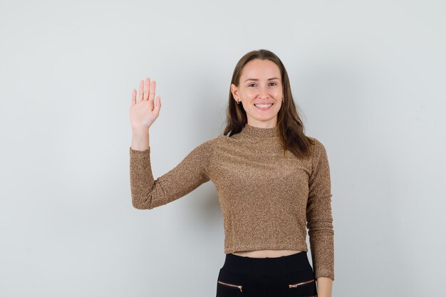 Jeune femme en chemisier, jupe en agitant la main pour au revoir et à la vue de face, sincère.