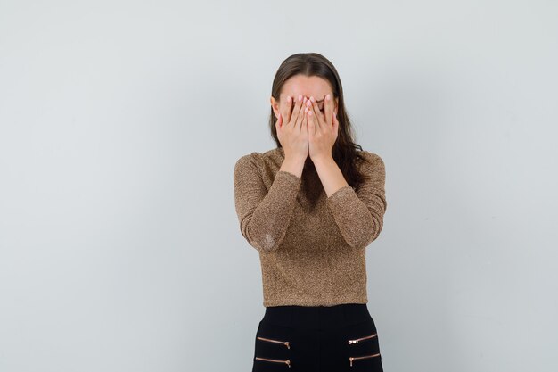 Jeune femme en chemisier, jupe couvrant le visage avec les mains et regardant troublé, vue de face.