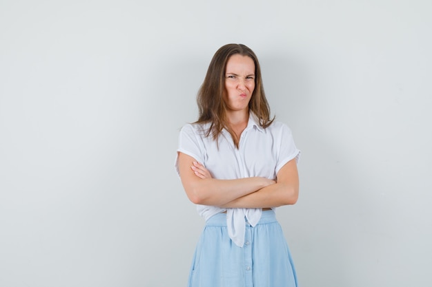 Jeune femme en chemisier, jupe debout avec les bras croisés tout en faisant la moue et à l'offensé