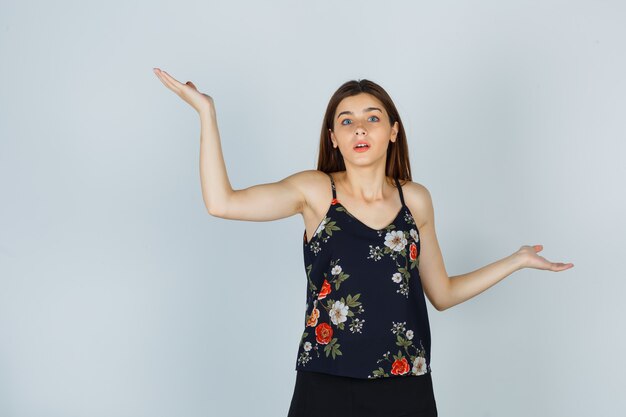 Jeune femme en chemisier, jupe montrant un geste impuissant et l'air perplexe, vue de face.