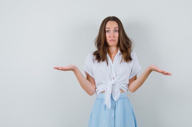 Jeune femme en chemisier et jupe montrant un geste impuissant et à la confusion