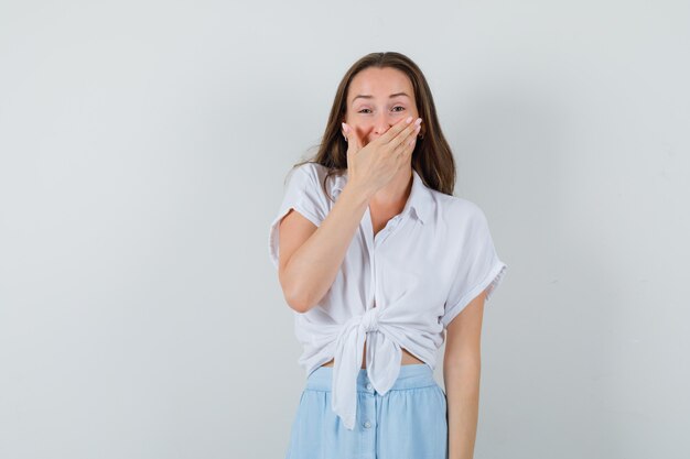 Jeune femme en chemisier et jupe souriant avec la main sur la bouche et à la joyeuse