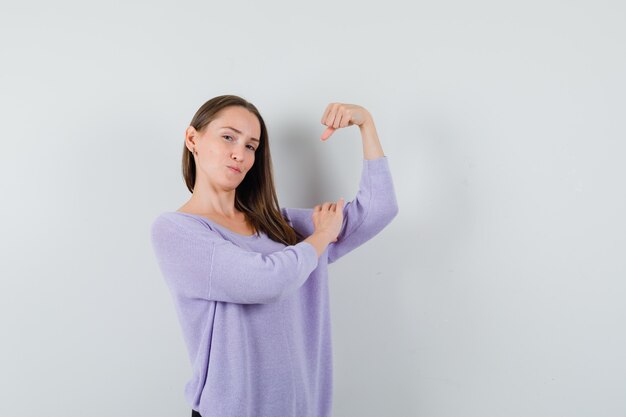 Jeune femme en chemisier lilas montrant ses muscles du bras et à la recherche de puissance