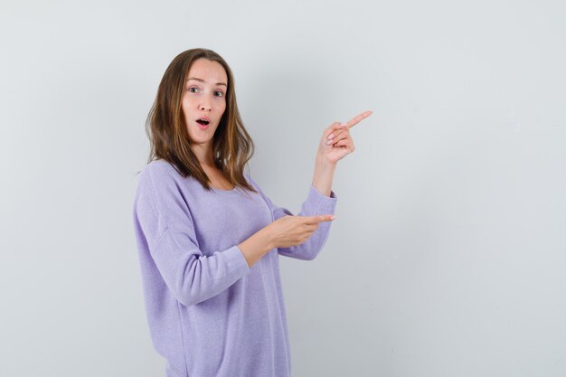 Jeune femme en chemisier lilas pointant de côté et à intéressé