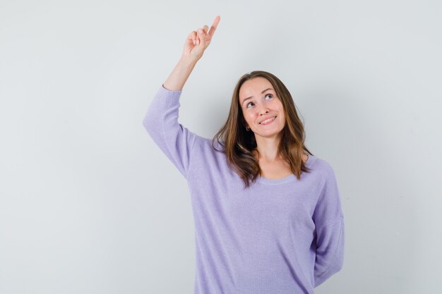 Jeune femme en chemisier lilas pointant vers le haut et à la recherche de plaisir