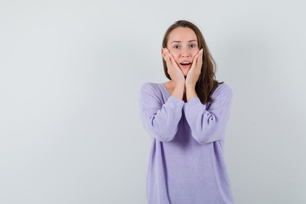 Jeune femme en chemisier lilas tenant les mains sur sa tête et à l'émotion