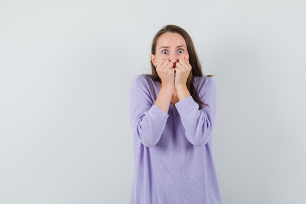 Jeune femme en chemisier lilas tenant les poings sur sa bouche et à l'excitation