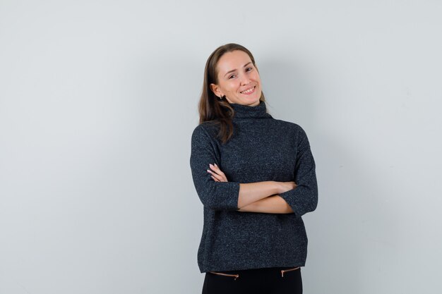 Jeune femme en chemisier noir debout avec les bras croisés tout en souriant et à la joie