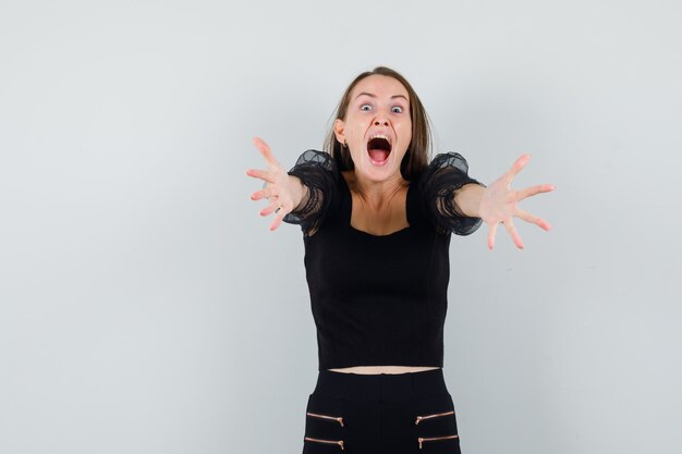 Jeune femme en chemisier noir levant les mains pour étreindre quelqu'un et à la joyeuse