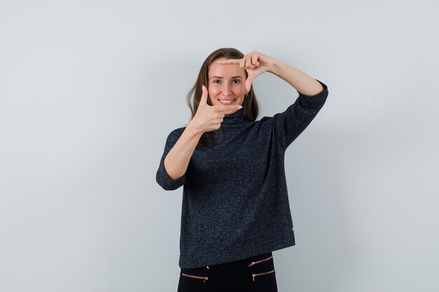 Jeune femme en chemisier noir montrant le geste du cadre et à la joyeuse