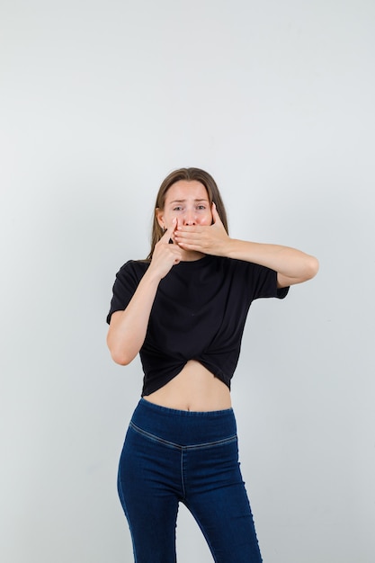 Jeune femme en chemisier noir, pantalon couvrant la bouche, pointant vers le sac pour les yeux et à la triste