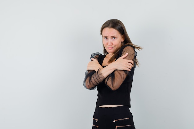 Jeune femme en chemisier noir et pantalon noir frissonnant de froid et à la jolie