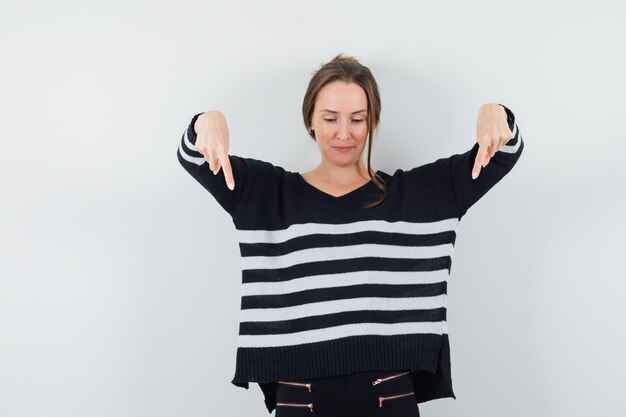 Jeune femme en chemisier noir et pantalon noir pointant vers le bas avec l'index et à l'optimiste