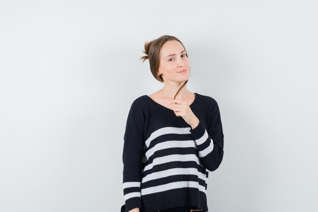 Jeune femme en chemisier noir et pantalon noir tenant une partie des cheveux d'une main et souriant et à la recherche de bonheur