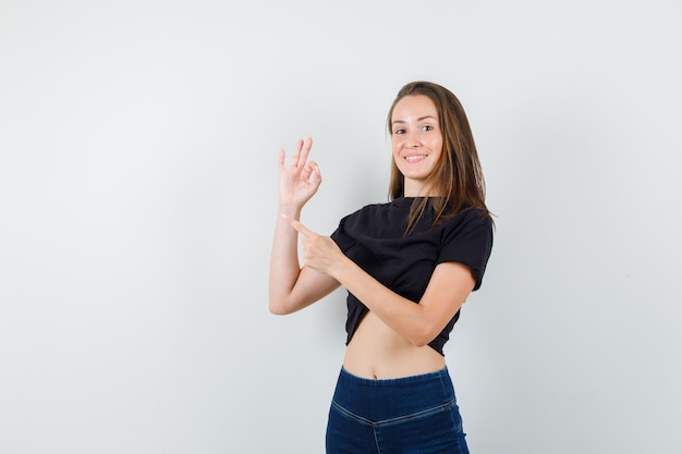 Jeune femme en chemisier noir, pantalon pointant vers l'extérieur avec signe ok et à la bonne humeur