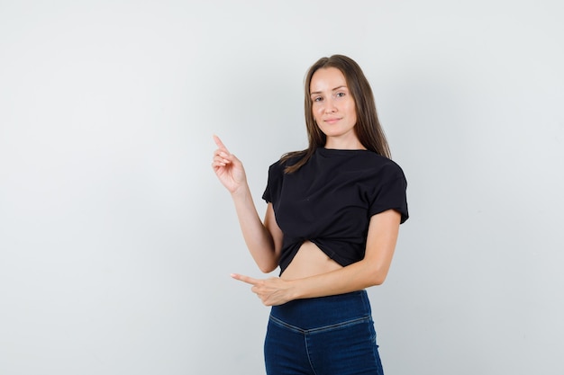 Photo gratuite jeune femme en chemisier noir, pantalon pointant vers le haut et à la certitude