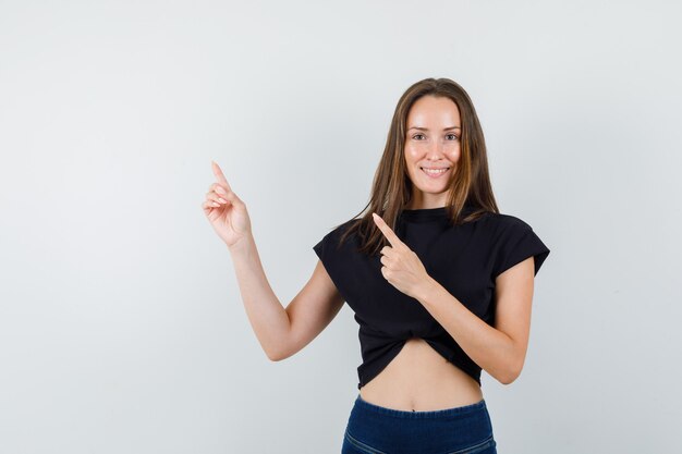 Jeune femme en chemisier noir pointant de côté et à la joyeuse