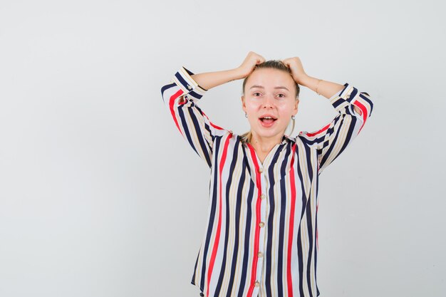 Jeune femme en chemisier rayé couvrant sa tête avec les mains et à la surprise