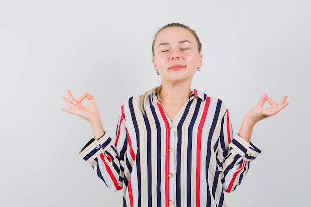 Photo gratuite jeune femme en chemisier rayé méditant et souriant et à la détente