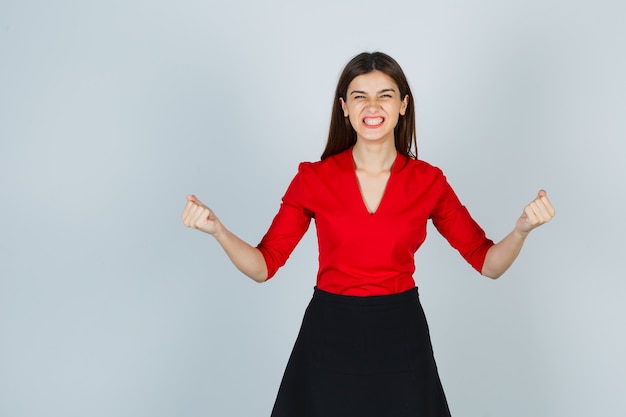 Jeune femme en chemisier rouge, jupe noire montrant le geste du gagnant et l'air heureux