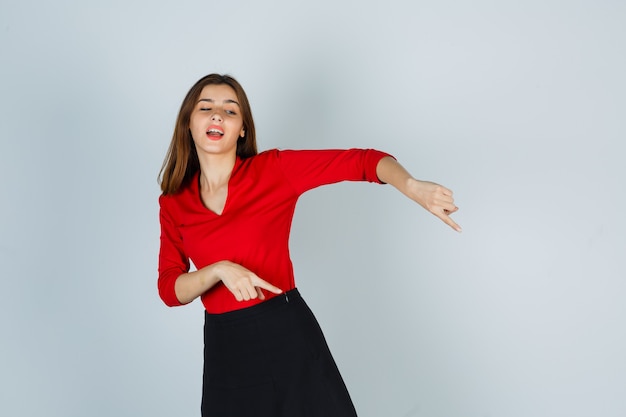 Jeune femme en chemisier rouge, jupe pointant vers le bas et l'air heureux