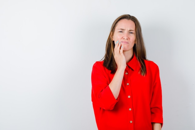 Jeune femme en chemisier rouge souffrant de maux de dents et semblant douloureuse, vue de face.