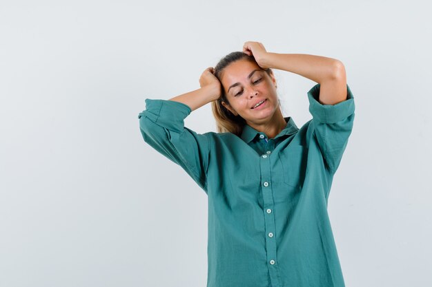 Jeune femme en chemisier vert, main dans la main sur la tête et à la pensive