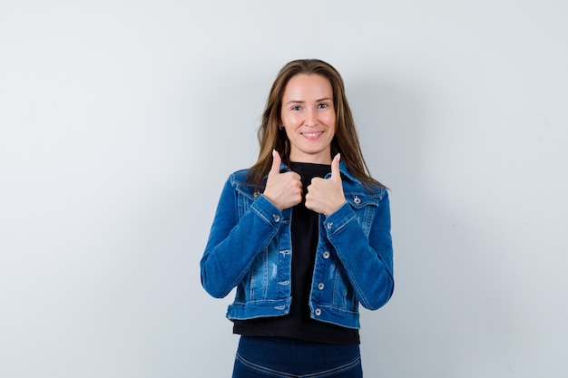 Jeune femme en chemisier, veste montrant le double pouce vers le haut et l'air confiant, vue de face.
