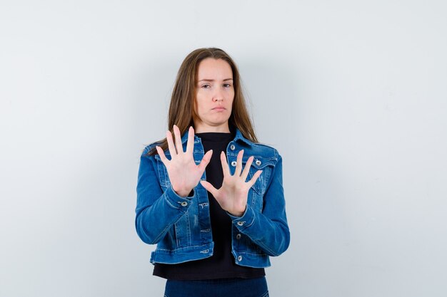 Jeune femme en chemisier, veste montrant un geste d'arrêt et l'air confiant, vue de face.