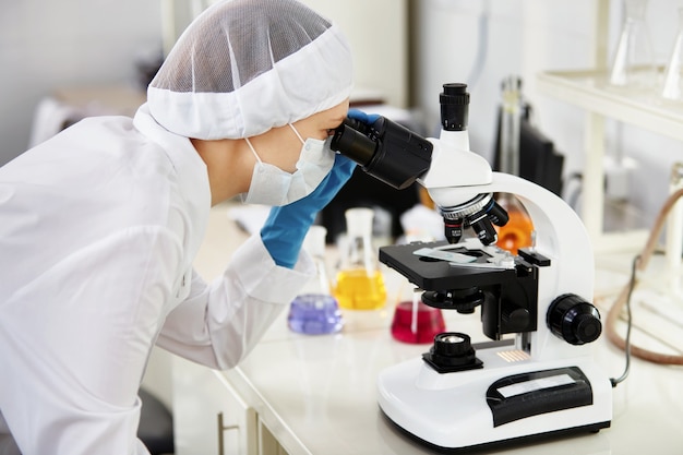 Jeune femme chercheur en médecine à la recherche à travers une lame de microscopie dans les sciences de la vie