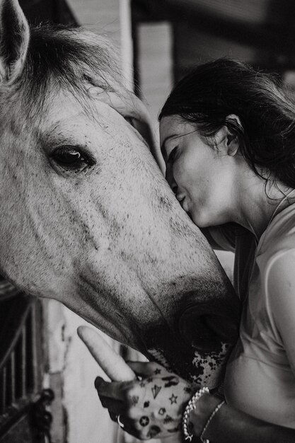 Une jeune femme et un cheval, des sentiments, des soins, de l'affection, de la tendresse, une femme câline et embrasse un cheval. Gros plan d'une jeune femme heureuse étreignant son cheval.