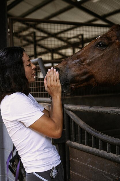 Une jeune femme et un cheval, des sentiments, des soins, de l'affection, de la tendresse, une femme câline et embrasse un cheval. Gros plan d'une jeune femme heureuse étreignant son cheval.