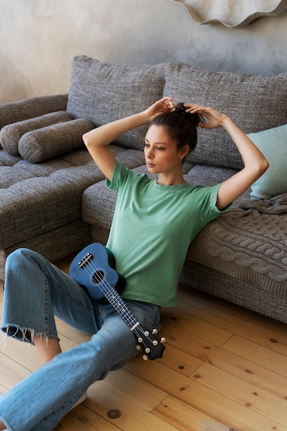 Photo gratuite jeune femme avec chignon désordonné jouant du ukulélé