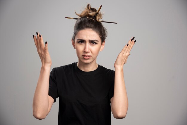 Jeune femme avec chignon en désordre debout sur un mur gris.