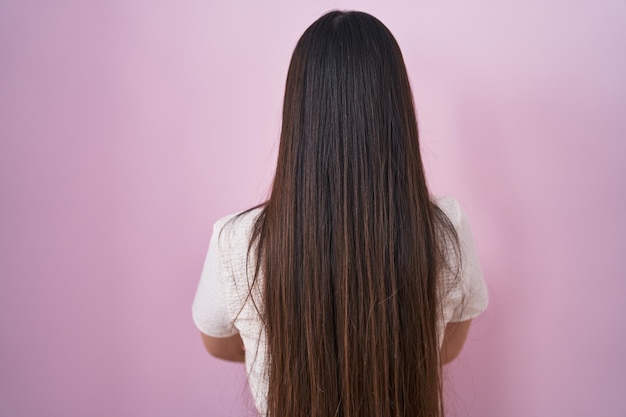 Photo gratuite jeune femme chinoise debout sur fond rose debout en arrière regardant loin avec les bras croisés