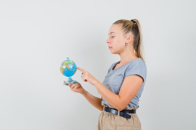 Jeune femme choisissant la destination sur le globe en t-shirt, pantalon et à la pensif.