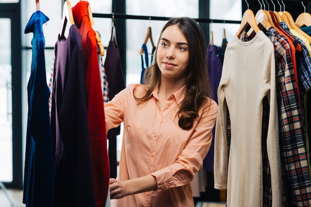 Jeune femme en choisissant des robes en magasin