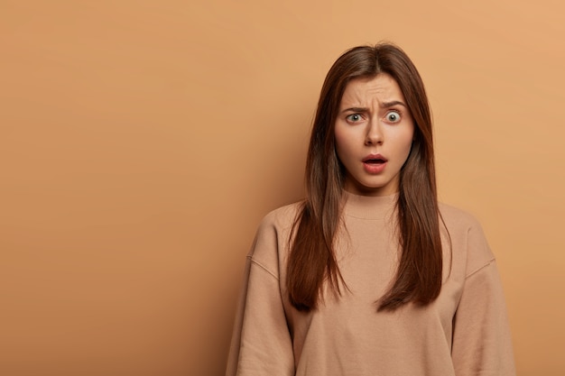 Une jeune femme choquée et embarrassée entend une rumeur époustouflante, fronce les sourcils, halète d'émerveillement avec la bouche grande ouverte