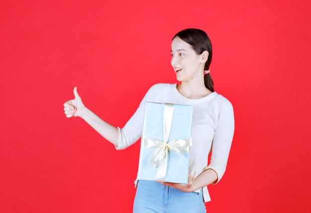 Jeune femme choquée tenant une boîte-cadeau et faisant des gestes vers le haut