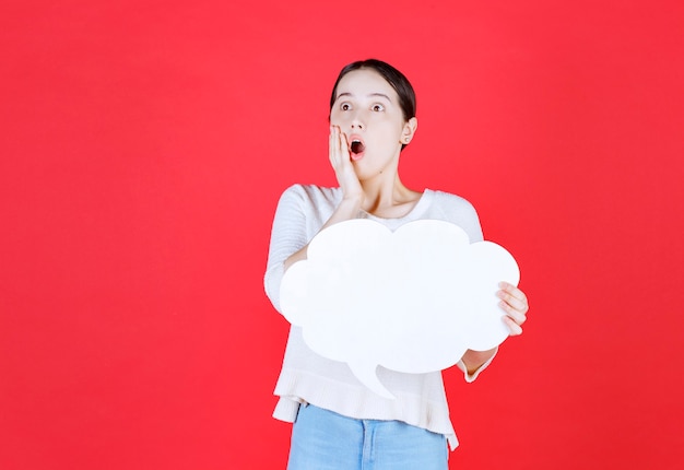 Jeune femme choquée tenant le conseil d'idée et regardant loin la bouche ouverte