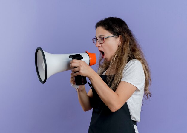 Jeune femme de coiffeur professionnel en tablier criant au mégaphone d'être frustré