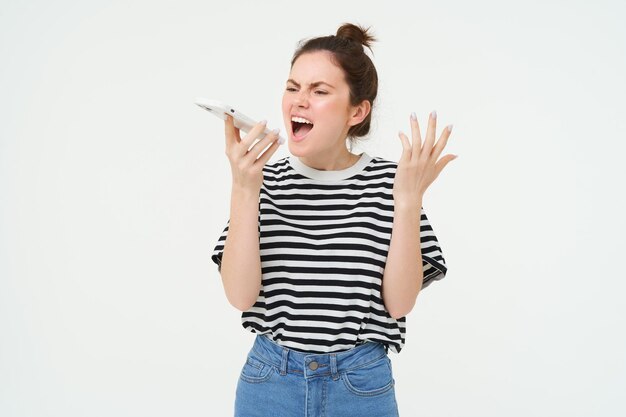 Photo gratuite une jeune femme en colère crie au haut-parleur, crie au téléphone portable et se serre la main debout.