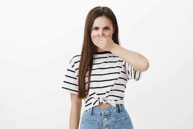 Jeune femme en colère ferme la bouche et fronce les sourcils, folle de parler