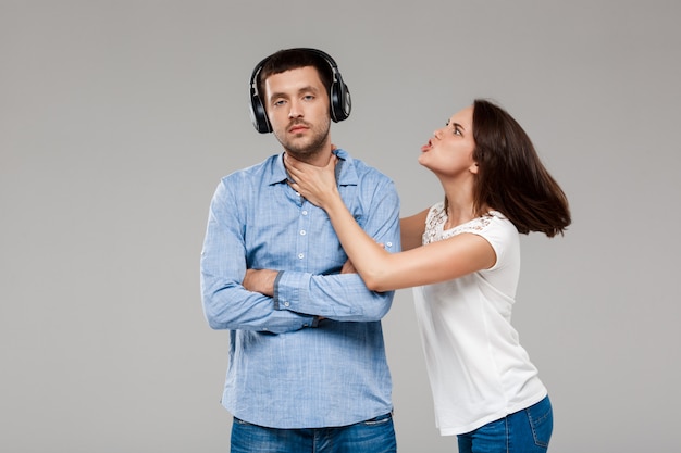 Jeune femme, colère, à, homme, dans, écouteurs, sur, mur gris