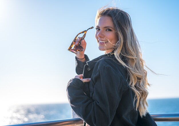 Jeune femme colombienne séduisante avec des lunettes de soleil posant debout au bord de la mer pendant la journée