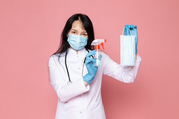 Jeune femme en combinaison médicale blanche gants bleus masque de protection bleu avec stéthoscope sur rose