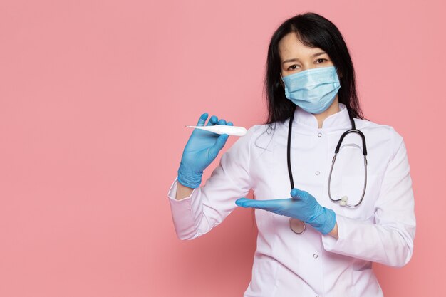 Jeune femme en combinaison médicale blanche gants bleus masque de protection bleu avec stéthoscope sur rose