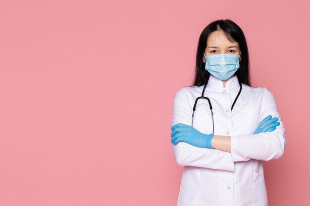 Jeune femme en combinaison médicale blanche gants bleus masque de protection bleu avec stéthoscope sur rose