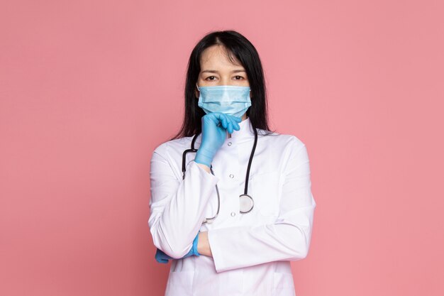 Jeune femme en combinaison médicale blanche gants bleus masque de protection bleu avec stéthoscope sur rose